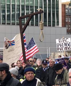 A group of people on a demonstration in London with a noose hanging from a wooden gallows being carried by one demonstrator. Another demonstrator is holding an American flag, another a banner saying "BBC: fake news, fake views".