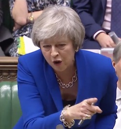 Theresa May, a late middle-aged white woman with grey hair wearing a royal blue jacket, standing up from the government front bench of the House of Commons waving her finger at Jeremy Corbyn.