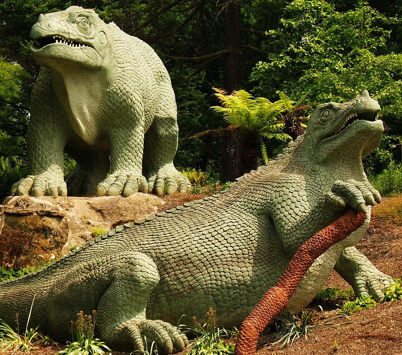 Statues of two iguanadons on rocks in a public park.