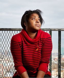 Picture of Erica Garner, a Black woman wearing a red sweatshirt with thin black horizontal stripes running across it. She also has a red ribbon pinned to her chest.
