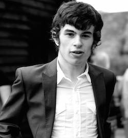 Black and white picture of Connor Sparrowhawk, a young white man wearing a dark-coloured suit jacket with a white shirt underneath