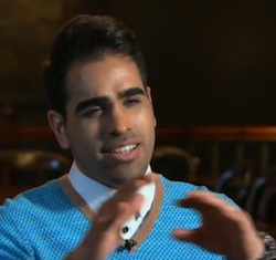 Picture of Dr Ranj Singh, a young South Asian man wearing a turcquoise V-neck sweater with a white shirt underneath, who has his hands raised in front of him as he speaks