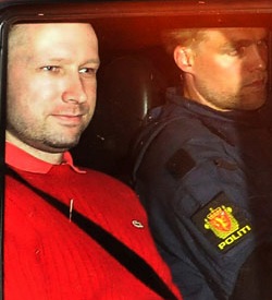 Anders Breivik accompanied by Norwegian policeman Anders Breivik in a red coat, being accompanied in a car by a Norwegian policeman with a red and gold badge with the word "Politi" underneath