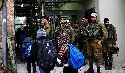 Three children with school bags entering a tunnel, passing by a group of armed Israeli soldiers.