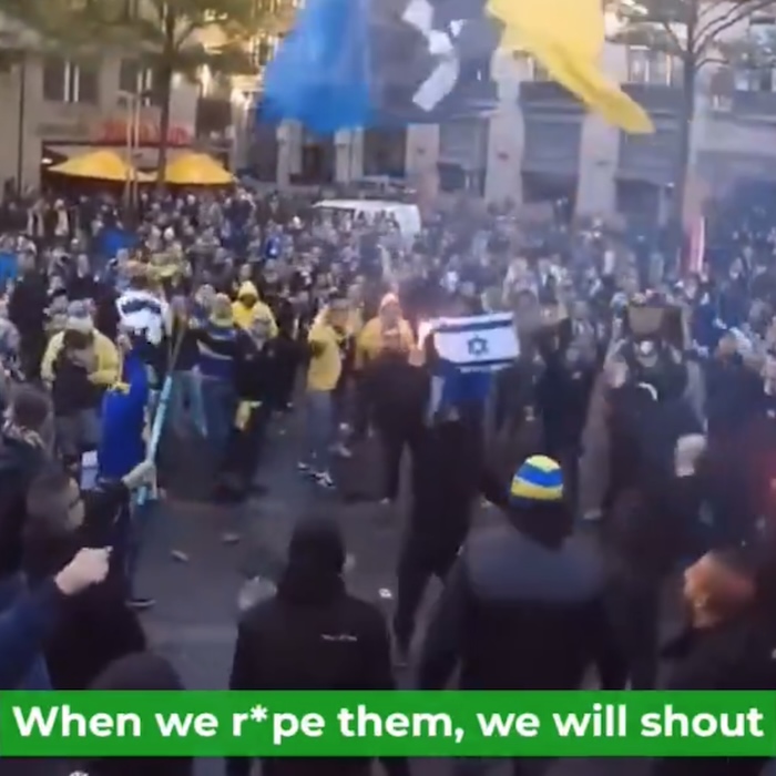 Still from a video of Maccabi Tel Aviv fans performing one of their chants. They are holding the club's flag and two Israeli flags can be seen in the crowd. The chant includes a threat of rape.